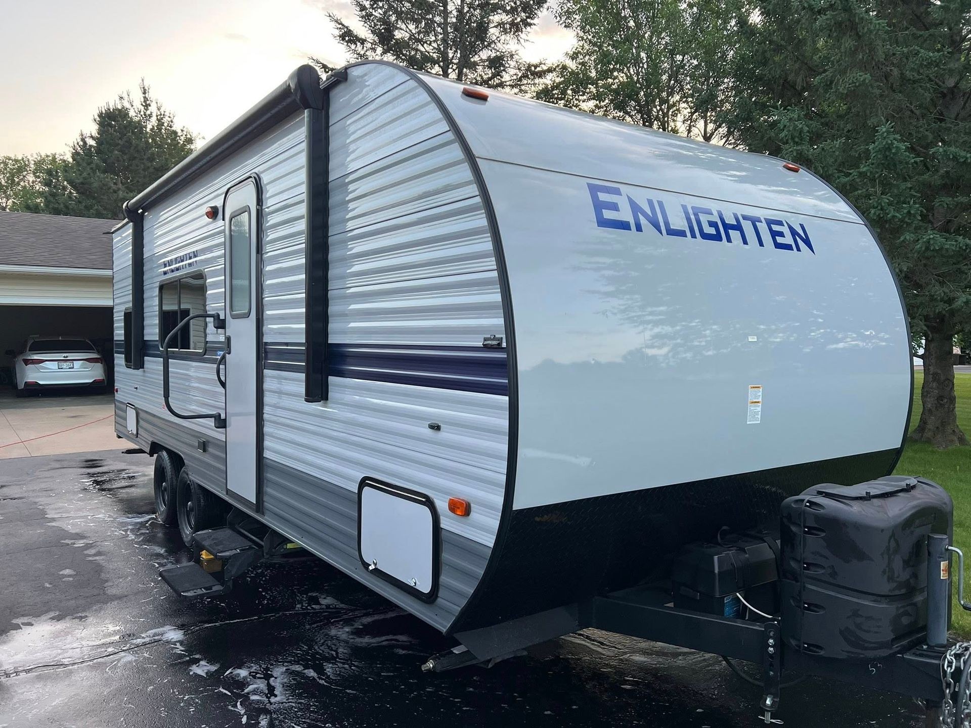 Gray travel trailer labeled 'ENLIGHTEN' parked in a driveway near a house and trees.